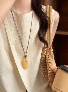Detailed view of a vintage marbled resin pendant necklace worn on a cream linen outfit.