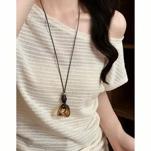 Detail of retro long necklace with amber resin pendant worn on a beige knit top
