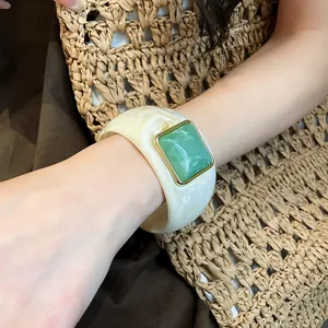 Dettaglio di un ampio bracciale in acrilico crema con pietra quadrata marmorizzata verde.