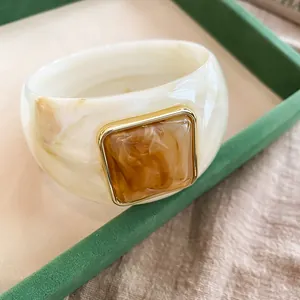 Dettaglio di un ampio bracciale in acrilico marmorizzato con inserto ambra