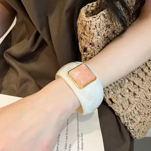 Dettaglio di un ampio bracciale in acrilico bianco marmo con pietra rosa quadrata al polso
