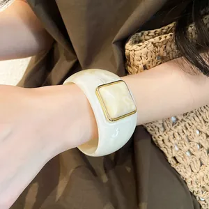 Vista dettagliata di un ampio bracciale in acrilico bianco con dettaglio in marmo dorato