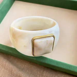 Primo piano di un ampio bracciale in acrilico marmorizzato con dettaglio quadrato dorato.