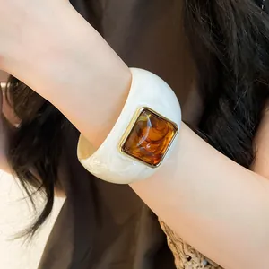 Dettaglio di bracciale largo in acrilico crema con intarsio in resina ambra e bordo oro