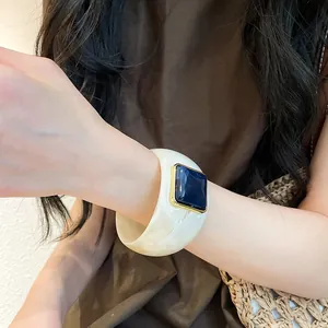 Primo piano dettagliato di un ampio bracciale in acrilico marmorizzato con gemma blu incastonata