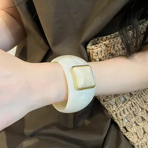 Dettaglio di un ampio bracciale rigido in acrilico bianco con decorazione quadrata