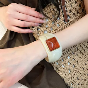 Primo piano di un ampio bracciale in acrilico marmorizzato con inserto quadrato marrone.