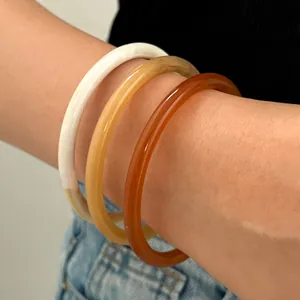 Primer plano de tres brazaletes de resina traslúcida en blanco, ámbar y caramelo.