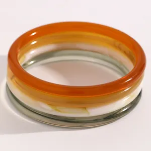 Primer plano de tres pulseras apilables de resina en color caramelo, blanco y gris humo.