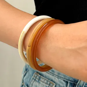 Primer plano de tres brazaletes de resina apilables en blanco hielo y color caramelo
