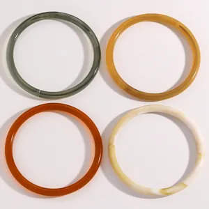 Primer plano de cuatro pulseras finas de resina en tonos tierra e imitación de jade.