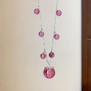 Detalle de un collar de cadena plateada con esferas de resina rosa traslúcida.