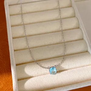 Macro detail of a silver necklace featuring a sparkling square blue zircon pendant