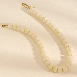 Close-up of cream-white beaded necklace with gold chain on textured background