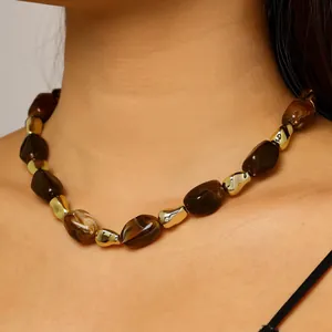 Detailed view of chunky brown marbled beads and gold polished metal necklace on model