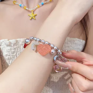 Dettaglio di un bracciale di perline con cuore in resina e ciondolo ciliegia sul polso