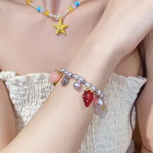 Dettaglio del braccialetto di perline stile resort con ciondoli a fragola e perle