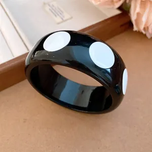 Macro detail of a black resin bangle with white polka dots for a minimalist look