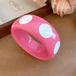Close-up of a glossy pink resin bangle featuring a stylish white polka dot pattern