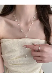 Delicate detail of French Y-shaped silver necklace with starry small pearls on model's neck