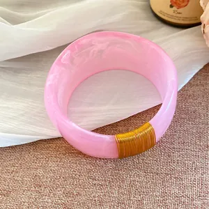 Bracelet en résine rose marbrée avec détails de fil doré élégants sur fond texturé