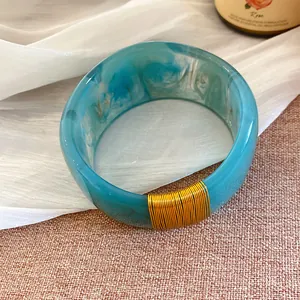 Détail d'un large bracelet en résine marbrée bleue avec une décoration en fil doré