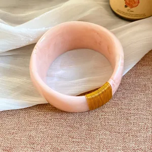 Vue détaillée d'un bracelet en résine marbrée rose avec enroulement de fil d'or.