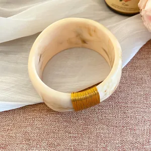Détail d'un large bracelet en résine marbrée avec un détail élégant de fil doré