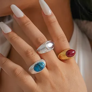 Dettaglio in primo piano di anelli plissettati placcati oro 18 carati con pietre colorate.