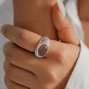 Dettaglio di un anello argentato a trama pieghettata con pietra ovale traslucida.