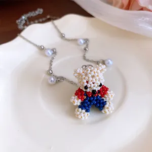 Close-up of a handmade beaded teddy bear pendant with pearls on a silver chain.