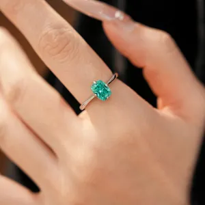 Gros plan d'une élégante bague géométrique en zircone vert émeraude sur un doigt.