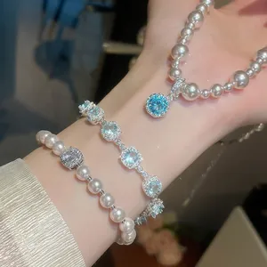 Vista dettagliata di collana e bracciale di perle con ciondoli in zircone blu su mano.