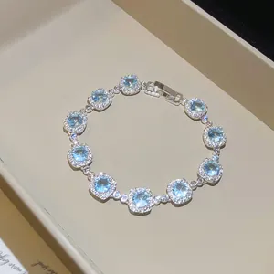 Primo piano del bracciale con zirconi blu chiaro e incastonatura halo in un vassoio beige
