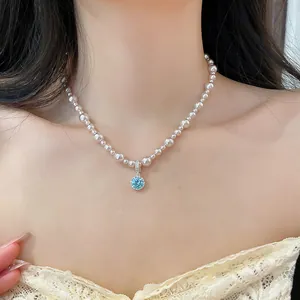 Primo piano di un'elegante collana di perle con ciondolo in zircone blu brillante al collo.