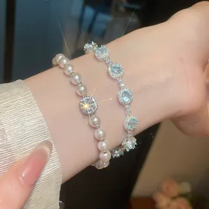 Dettaglio di un elegante bracciale di perle e catena di zirconi su un polso femminile.