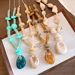 Close-up of four colors of marble-patterned acrylic oval pendant necklaces on a wooden tray.