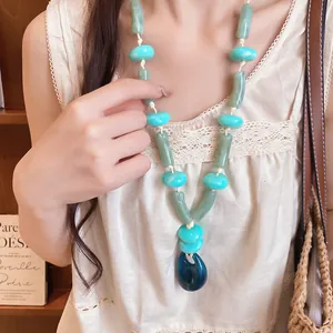Close-up view of an acrylic bead necklace with dark blue teardrop pendant on a model