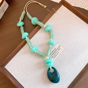 Detailed macro view of an acrylic resin necklace with teal beads and oval pendant.