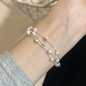 Detailansicht eines zweilagigen Perlenarmbands mit Silberperlen am Handgelenk.