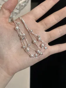 Detailansicht eines mehrlagigen Silberarmbands mit Perlen, in der Hand gehalten.