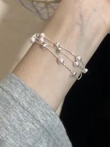 Detailansicht eines mehrlagigen silberfarbenen Armbands mit Perlen am Handgelenk
