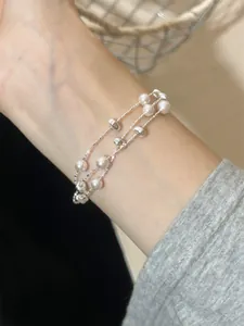 Detailansicht eines eleganten mehrlagigen Barockperlen- und Silberperlenarmbands am Handgelenk