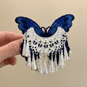 Macro detail of a vintage blue embroidered butterfly hair clip featuring silver tassels