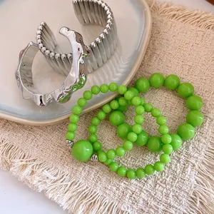 Close-up of green acrylic beaded bracelets and silver metallic bangles on a woven mat.