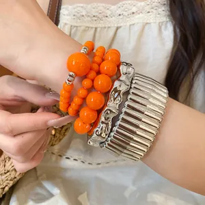 Close-up of stacked orange acrylic beads and chunky silver textured metallic bracelets.