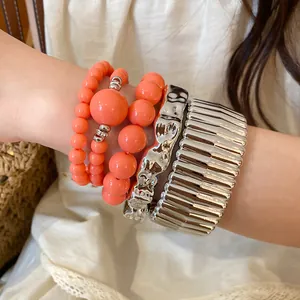 Detail shot of bohemian orange acrylic beaded bracelets and silver textured cuffs on wrist.