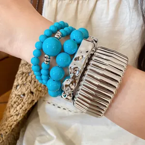 Detailed view of stacked turquoise acrylic beaded bracelets and silver metallic bangles