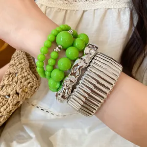 Close-up detail of layered green acrylic beaded bracelets and chunky metallic silver bangles