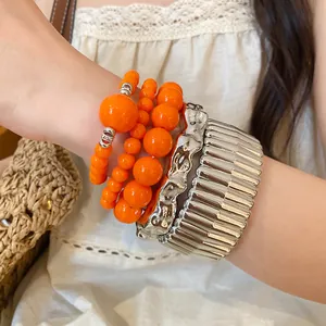 Detail view of orange acrylic beaded bracelets paired with a textured silver metal cuff